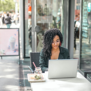 A Black woman sits outside while working on a laptop